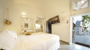 Une chambre à coucher comprenant un lit, un téléviseur fixé au mur, une porte donnant sur un balcon et une petite fenêtre.