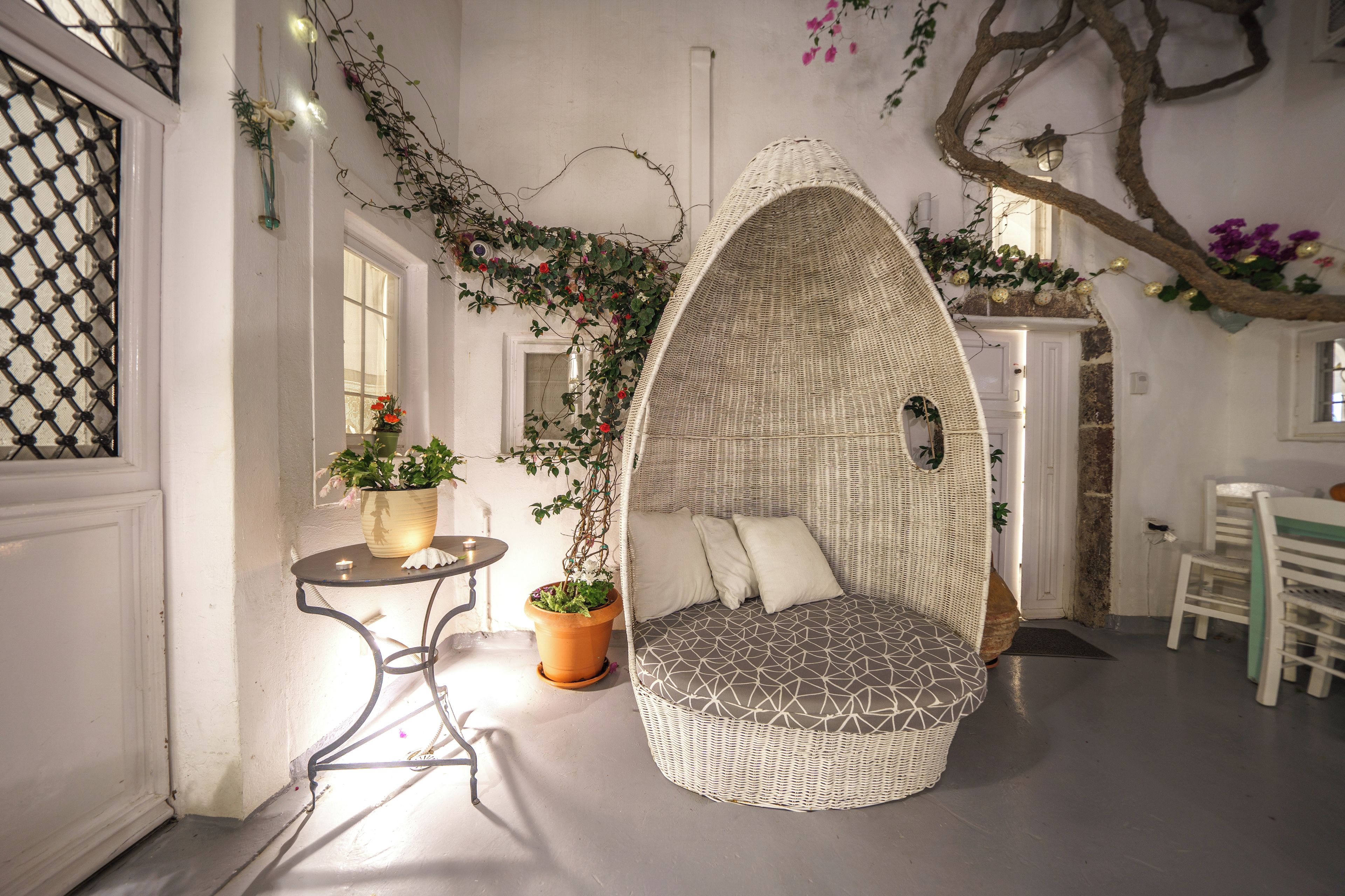A cozy interior with a wicker hanging chair, a small table with a candle, and potted plants.