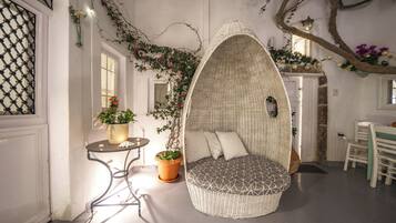A cozy interior with a wicker hanging chair, a small table with a candle, and potted plants.