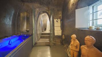 Ein Wellnessbereich mit einem blauen, beheizten Pool, Steinwänden und einer Treppe zu einer erhöhten Ebene.