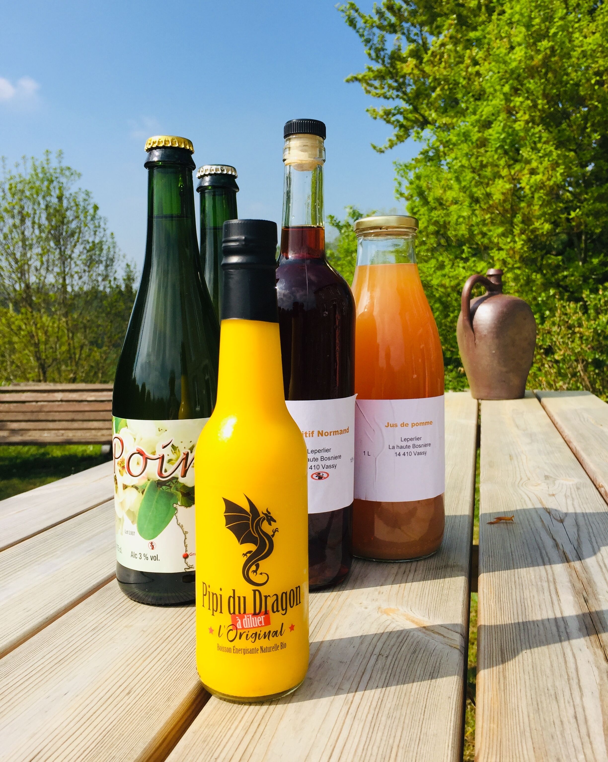 Une table en bois sur laquelle sont posées quatre bouteilles de boissons et une cruche en céramique.