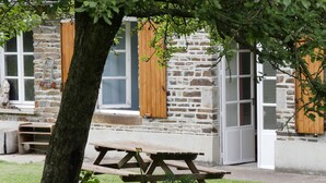 A stone building with wooden shutters, a wooden bench, and a picnic table in a grassy area. - Small house o waterfront. (Valdallière)