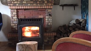 A fireplace with a brick surround, a log stack, and a wooden stool. - Small house o waterfront. (Valdallière)