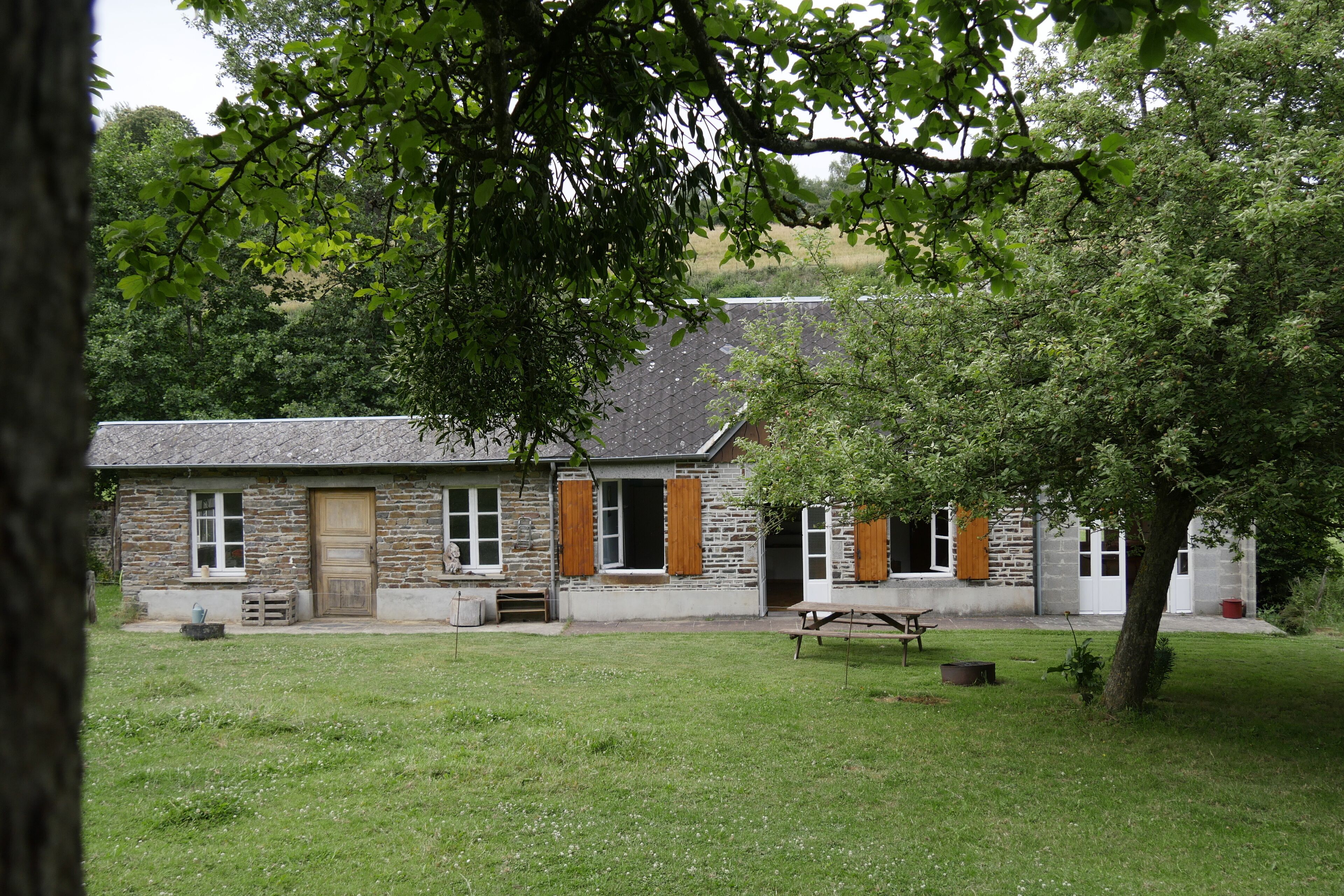 A stone building with a sloped roof, a grassy yard, and a tree in the foreground.