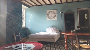 A room with a bed, a table, a chair, a lamp, and a wall with a circular design. - Small house o waterfront. (Valdallière)