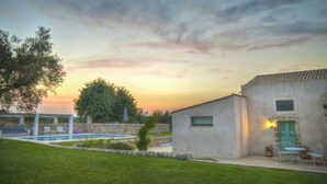 Zona de piscina con un muro de piedra, una pérgola y un pequeño edificio con una puerta verde.