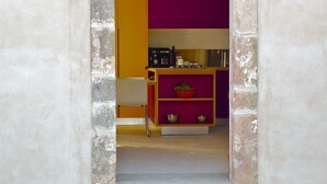 Una puerta que da a una habitación con área de cocina, un estante con utensilios y una pequeña mesa.