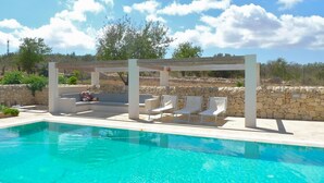 Un área de piscina con pérgola, sillas de descanso y un muro de piedra.
