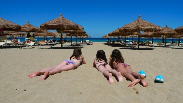Una playa con sombrillas de paja y sillas reclinables.