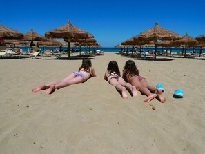 A beach with thatched umbrellas and lounge chairs.