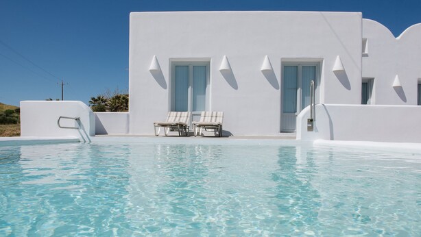 A pool area with two lounge chairs and a white building with doors and windows.