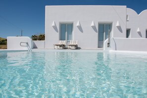 A pool area with two lounge chairs and a white building with doors and windows. - Sand Villa - sea front luxury villa by  Monolithos beach. (Έξω Γιαλός Καρτεραδου)