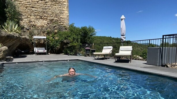 Una piscina con agua cristalina, rodeada de sillas de descanso y un muro de piedra.