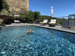 Una piscina con agua cristalina, rodeada de sillas de descanso y un muro de piedra.