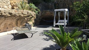 Un muro de piedra, una toldo blanco y una silla de lounge en un patio.