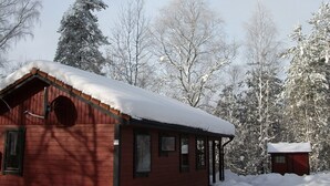 Une cabane en bois rouge, dont le toit est recouvert de neige, entourée d’arbres chargés de neige.