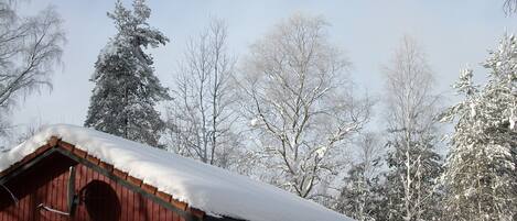 Eine rote Holzhütte mit einem schnee bedeckten Dach, umgeben von mit Schnee beladenen Bäumen.