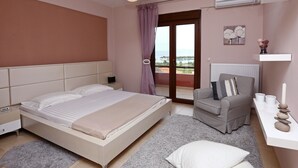 A bedroom with a bed, a chair, a bedside table, and a view of the outdoors. - Pefkochori villa with a stunning panoramic view and a waterfall private pool. (Pefkochori Chalkidiki)