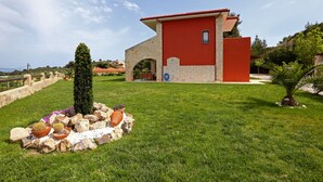 A modern house with a red and beige exterior, a stone archway, and a well-maintained lawn with cacti and rocks. - Pefkochori villa with a stunning panoramic view and a waterfall private pool. (Pefkochori Chalkidiki)