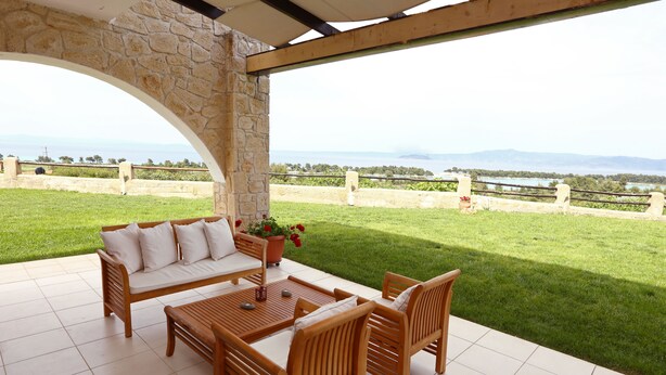A patio with a stone archway, a wooden sofa, and a table with chairs. - Pefkochori villa with a stunning panoramic view and a waterfall private pool. (Pefkochori Chalkidiki)