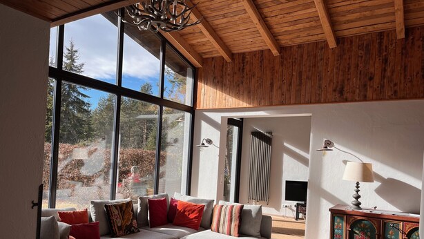 Ein modernes Wohnzimmer mit einem großen Fenster, einer Holzbalkendecke und einem Sofa mit bunten Kissen.