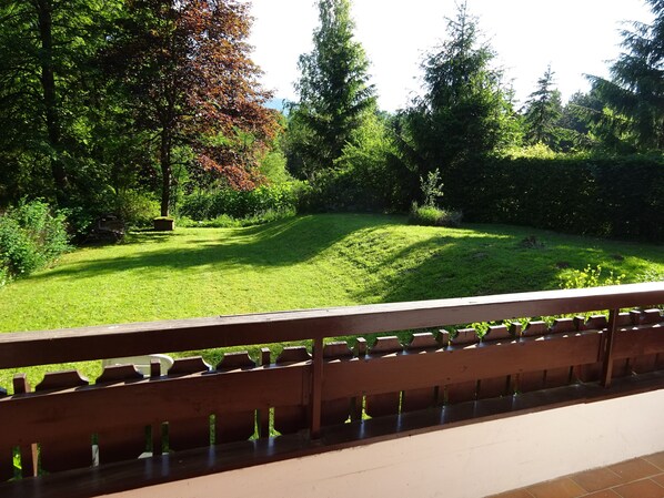 Un jardín con valla de madera, abundante vegetación y una zona de césped.