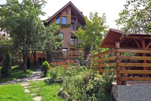 Una cabana de fusta amb un balcó, envoltada d'un jardí ple de plantes i flors diverses.