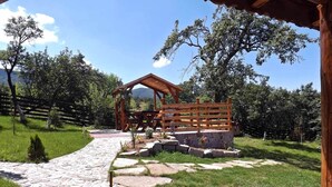 A stone pathway leading to a wooden gazebo with a picnic table, surrounded by lush greenery and a stone wall. - • CASA ZOLLO II • cosy studio apartment in a quaint Carpathian village, Sibiu (Sibiu)