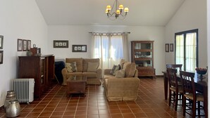 Un salón amplio con techo alto, una araña, un comedor con sillas de madera y suelo de baldosas.