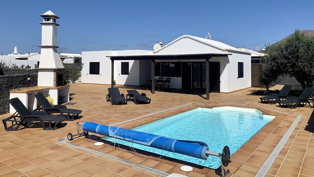 Una casa moderna con piscina, mobiliario exterior y chimenea.