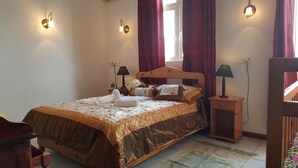 Un dormitorio con una cama de madera, dos mesitas de noche con lámparas, una ventana con cortinas rojas e iluminación empotrada en la pared.