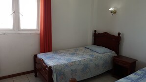 Una cama individual con colcha estampada, cabecera de madera, mesita de noche y lámpara de pared.