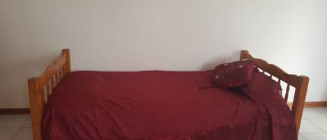 Una cama individual con estructura de madera y colcha roja.