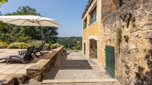 Un edificio de piedra con puerta verde, asientos exteriores con sombrillas y vistas al paisaje.