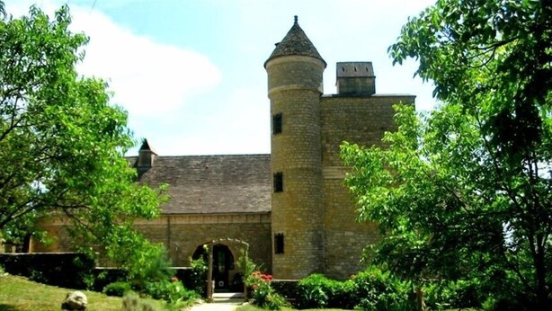 Un castillo de piedra con una torre central y una entrada en arco, rodeado de abundante vegetación.