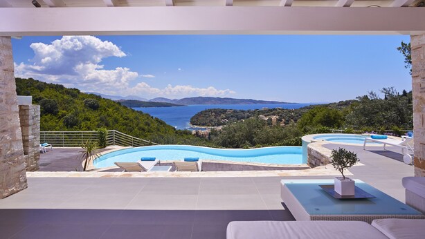 Un espace piscine extérieur moderne, doté de chaises longues, d’une petite table et offrant une vue sur la mer et les collines.