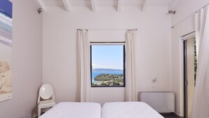 Une chambre avec deux lits, une vue sur la mer, une chaise blanche et un radiateur.