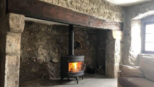 Ein Kamin aus Stein mit einem modernen Holzofen, eine Steinsäule und ein Sofa in einem gemütlichen Raum.