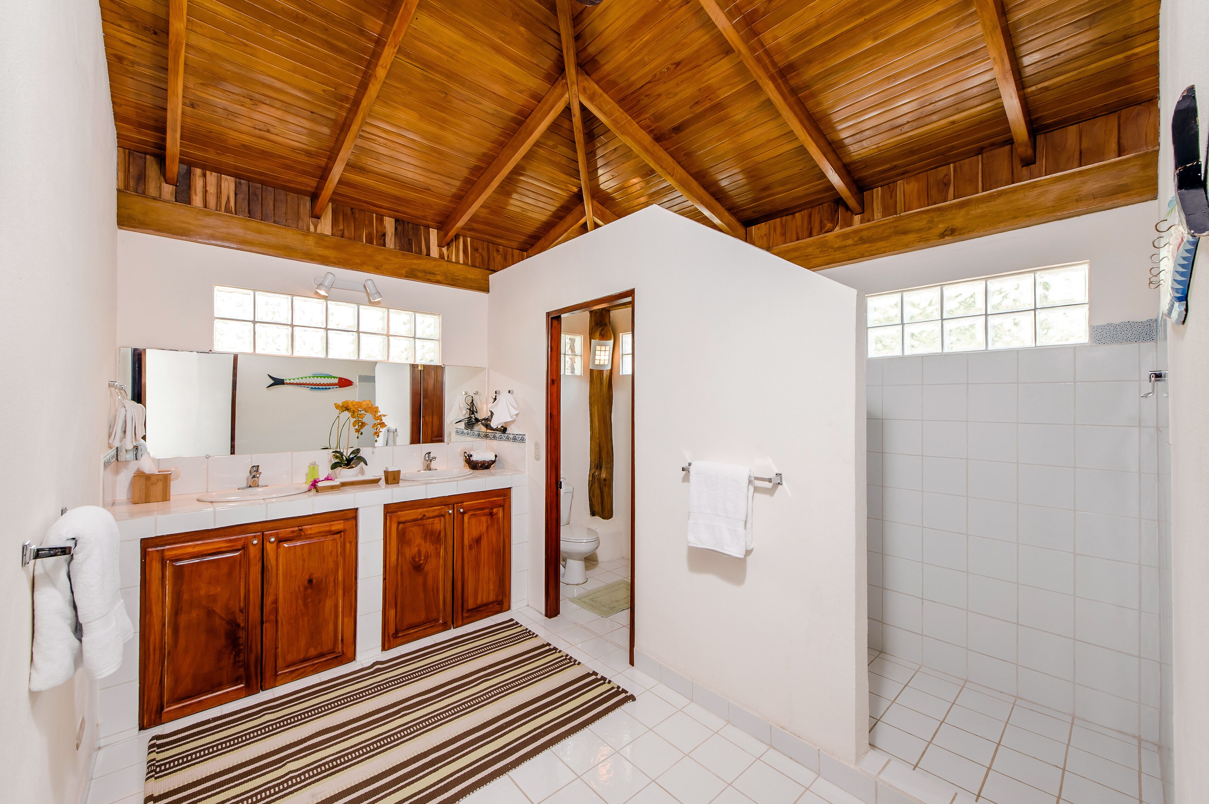 Une salle de bain avec des meubles en bois, un grand miroir, une douche et un sol carrelé.