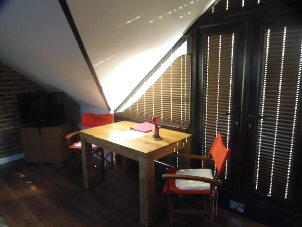 A dining area with a wooden table and chairs, a small red table lamp, and a window with blinds. - Detached 1st Floor Studio Flat (Wick)