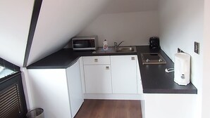 Una cocina compacta con microondas, lavamanos y cafetera.