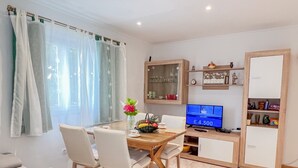 Ein modernes Wohnzimmer mit Esstisch, Stühlen, einer Couch, einem Fernseher und einem Schrank.