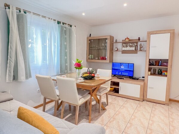 A modern living room with a dining table, chairs, a sofa, a TV, and a cabinet.