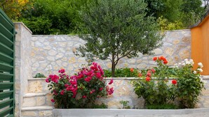 Un muro de piedra con un pequeño árbol y plantas con flores.