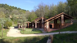 Edifici de construcció rústica amb façana de pedra i teulat inclinat, envoltat d'un jardí ben cuidat i arbres.