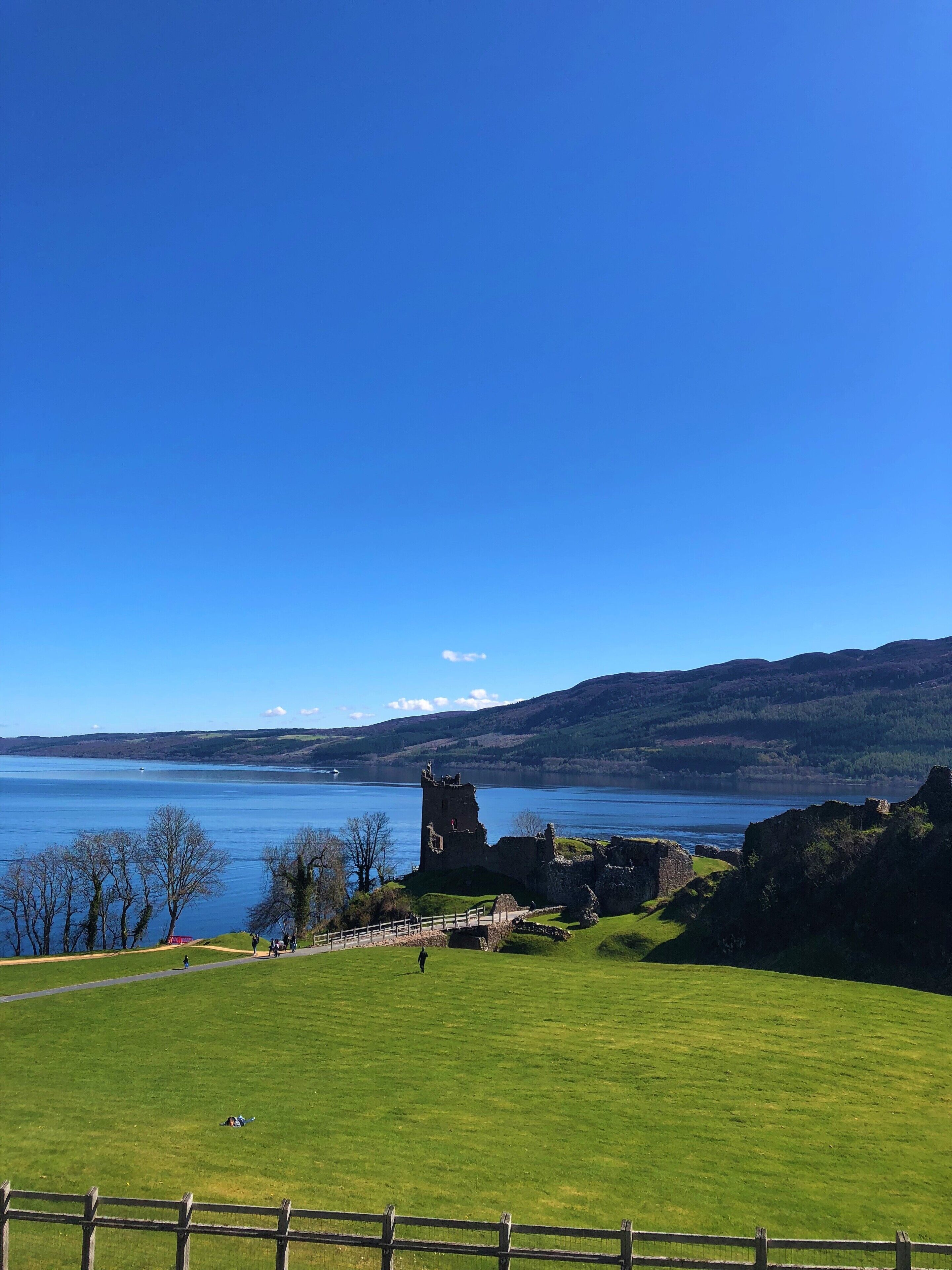 A historic castle ruin on a grassy hill overlooking a calm lake with distant hills.