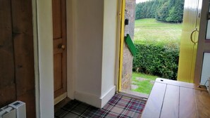 A hallway leading to a door with a view of a green landscape. - Traditional highland cottage with magnificent panoramic views  (invernesshire)