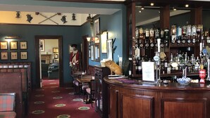 A bar area with a wooden counter, a variety of bottles, and framed pictures on the wall. - Traditional highland cottage with magnificent panoramic views  (invernesshire)