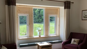A room with a large window, a wooden bench, a purple armchair, and a small table. - Traditional highland cottage with magnificent panoramic views  (invernesshire)