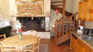 A rustic kitchen with wooden cabinets, a dining table with chairs, a fireplace, and a staircase. - The Country House Mijotiere (monestier)